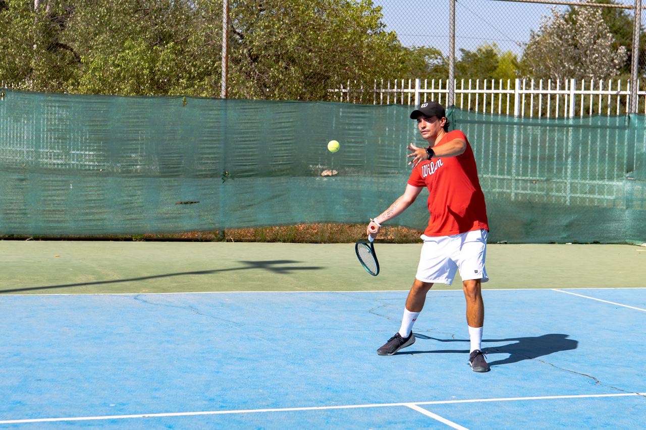 Rami en una pista de tenis, con camiseta roja y raqueta